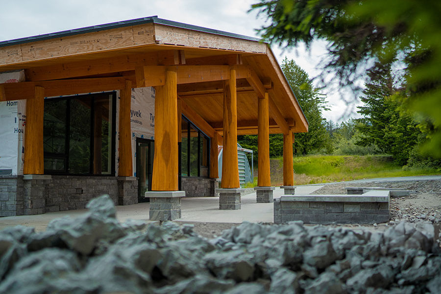 Side view of a Canadian timber frame commercial building by Smith Timber Works, showcasing sturdy wooden columns, stone bases, and a wide overhang, reflecting quality design and build in British Columbia.