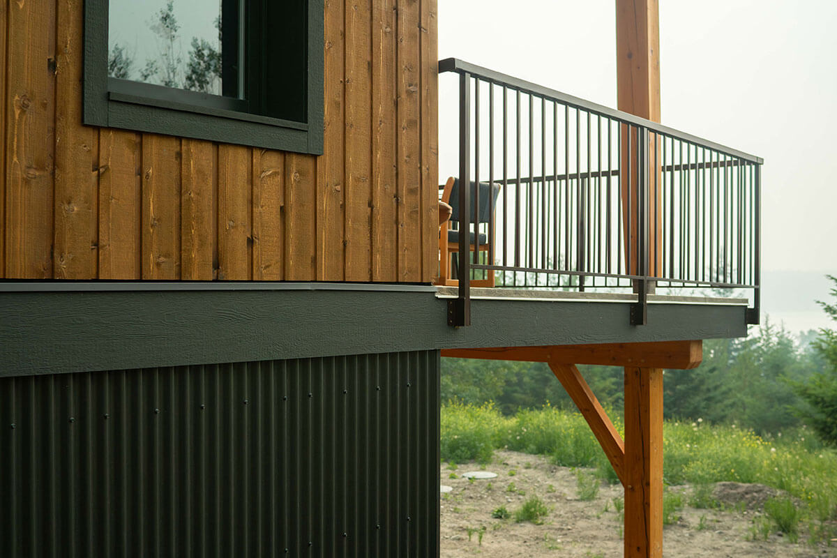 Close-up of timber frame balcony with vertical wood siding and black metal railing, crafted by Smith Timber Works.