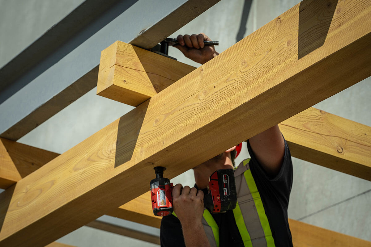 Construction worker using a power drill to secure large timber beams to a commercial building structure.