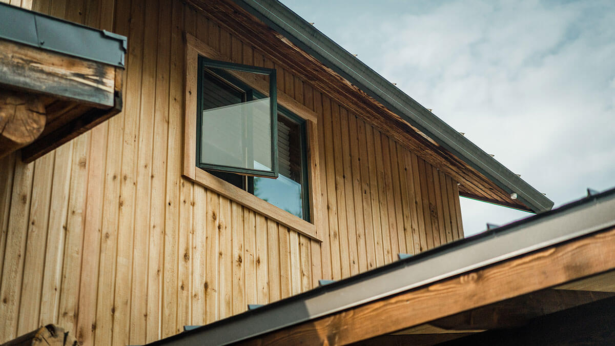 Detail of a Canadian timber frame home by Smith Timber Works, showcasing natural wood siding, an open window, and durable roofline, reflecting quality craftsmanship and attention to detail.
