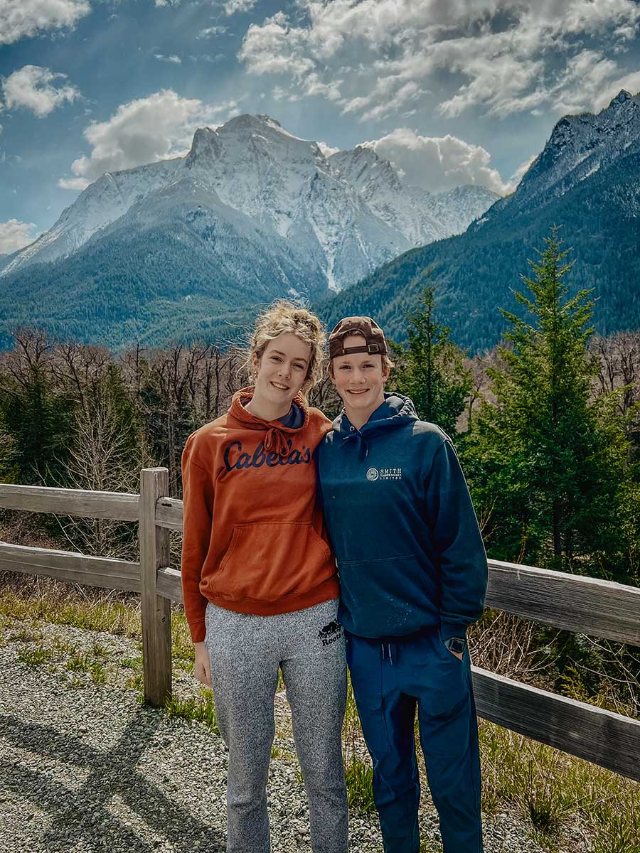 Two people standing in front of a scenic mountain backdrop in British Columbia, embodying the connection to nature valued by Smith Timber Works.