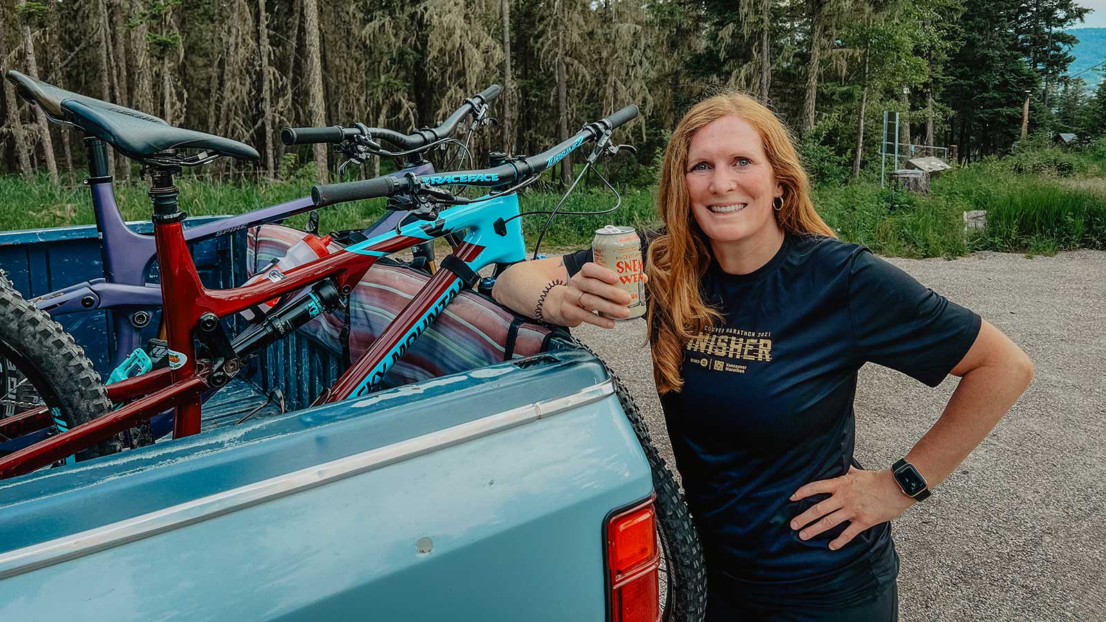 Woman enjoying a post-ride drink next to mountain bikes in a pickup, celebrating the active, outdoor lifestyle embraced by Smith Timber Works.