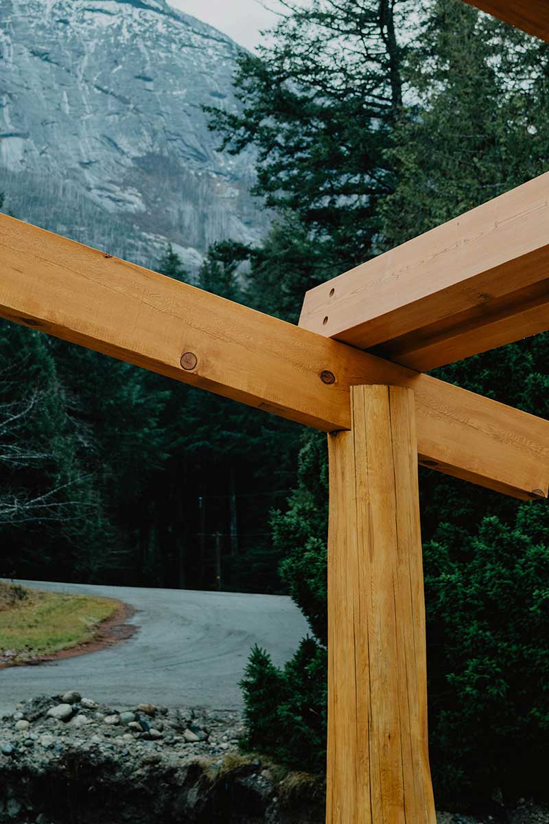Timber frame structure detail with a focus on a strong wooden joint and column, set against a mountainous and forested British Columbia background, highlighting Canadian craftsmanship by Smith Timber Works.