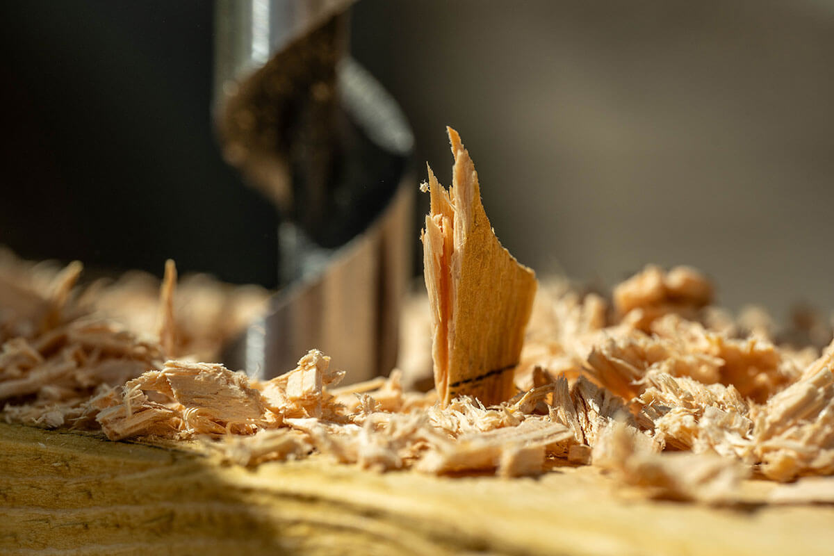 Close-up of a drill bit cutting into a piece of wood, creating sharp wood shavings.
