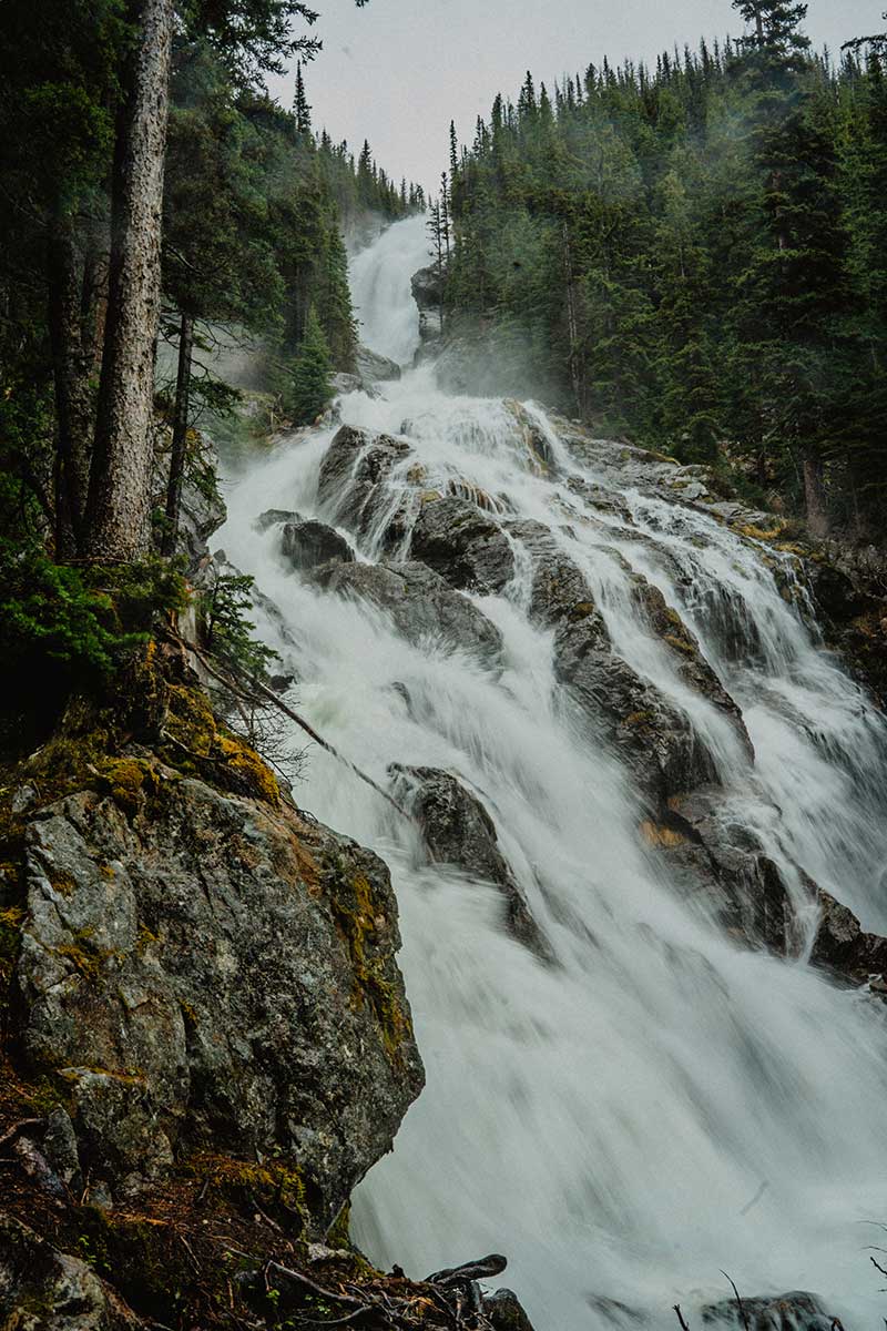Powerful mountain waterfall cascading through forested cliffs in British Columbia, reflecting the raw natural beauty that inspires Smith Timber Works.