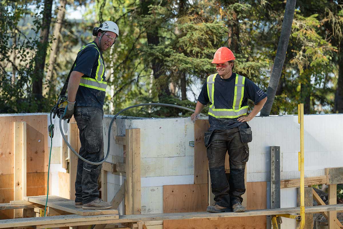 Smith Timber Works crew members on scaffolding during insulated concrete form (ICF) wall construction in a forested British Columbia job site.
