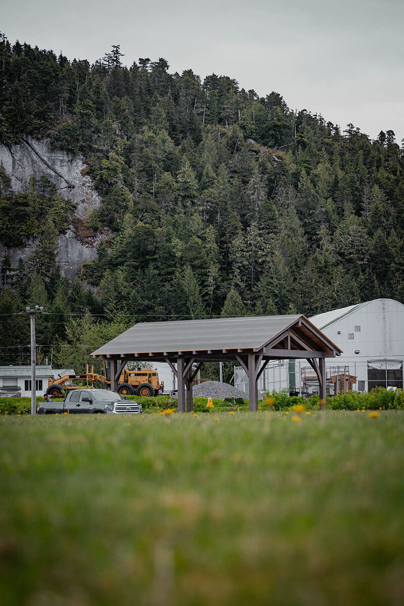 Outdoor timber frame shelter with a practical roof, built by Smith Timber Works, situated in a Canadian landscape near a wooded hillside.