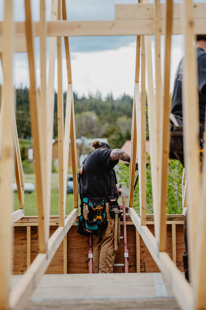 Carpenter framed by timber rafters on Smith Timber Works job site.