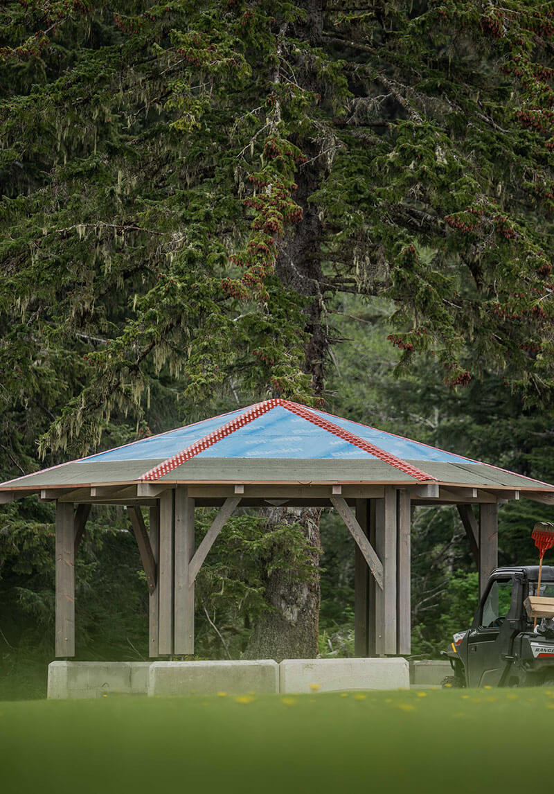 Outdoor timber frame gazebo with a distinct blue roof, built by Smith Timber Works, providing a versatile gathering space in a natural Canadian setting.