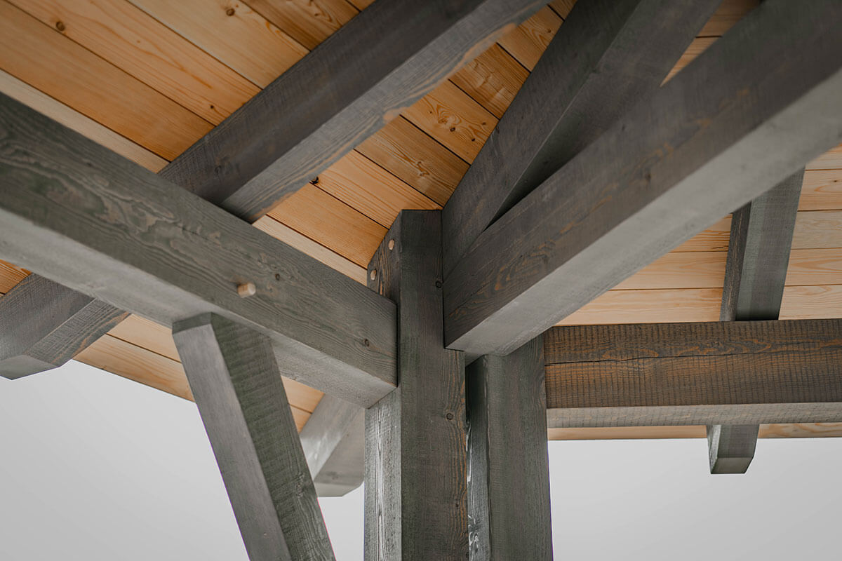 Interior view of a timber frame structure with visible joinery and a wood plank ceiling, showcasing the detailed craftsmanship of Smith Timber Works.