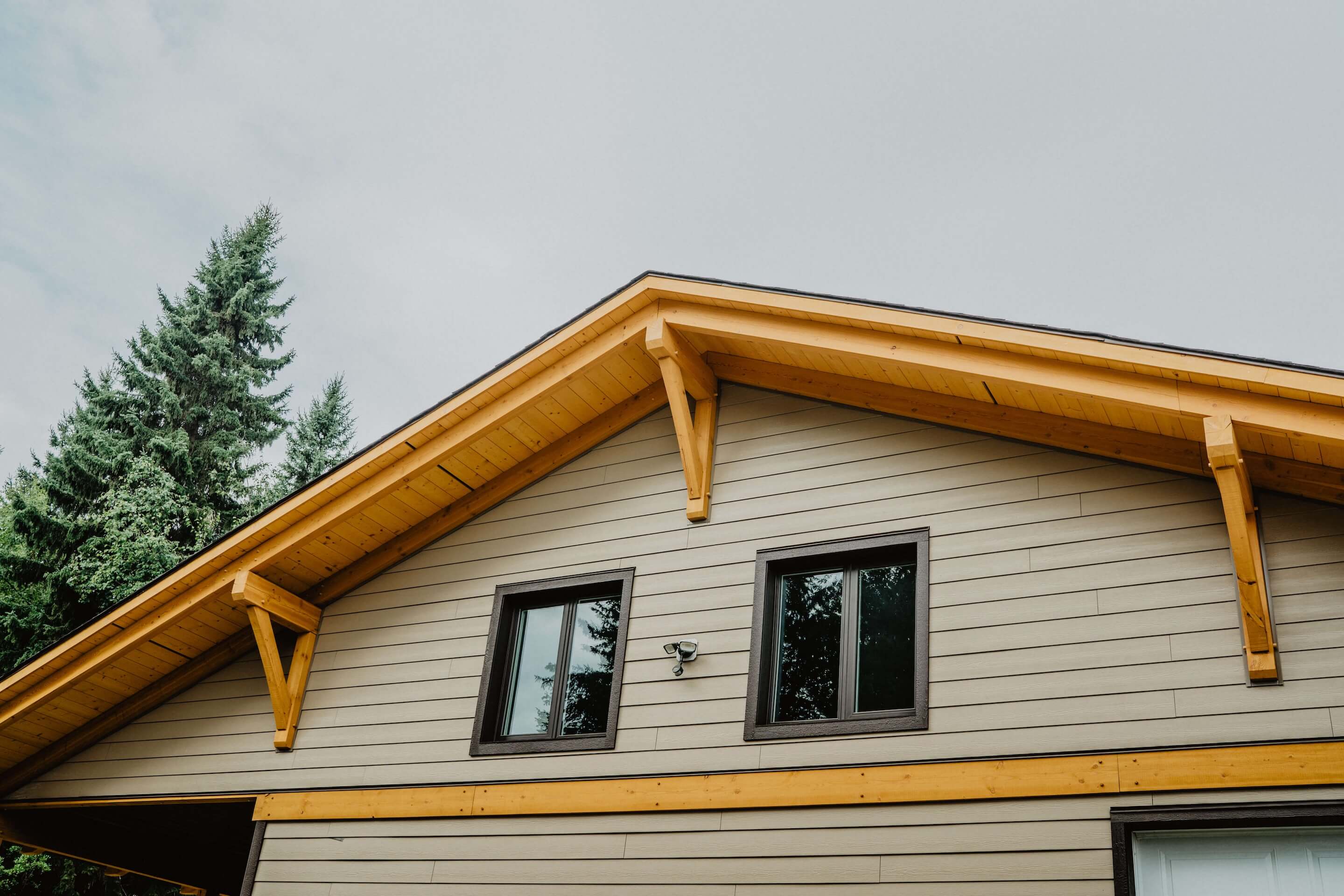 Gable end of a custom Canadian timber frame shop by Smith Timber Works, showcasing exposed rafter tails, knee braces, wood accents, and clean Hardie fibre cement siding, highlighting superior craftsmanship and design. In the BC interior