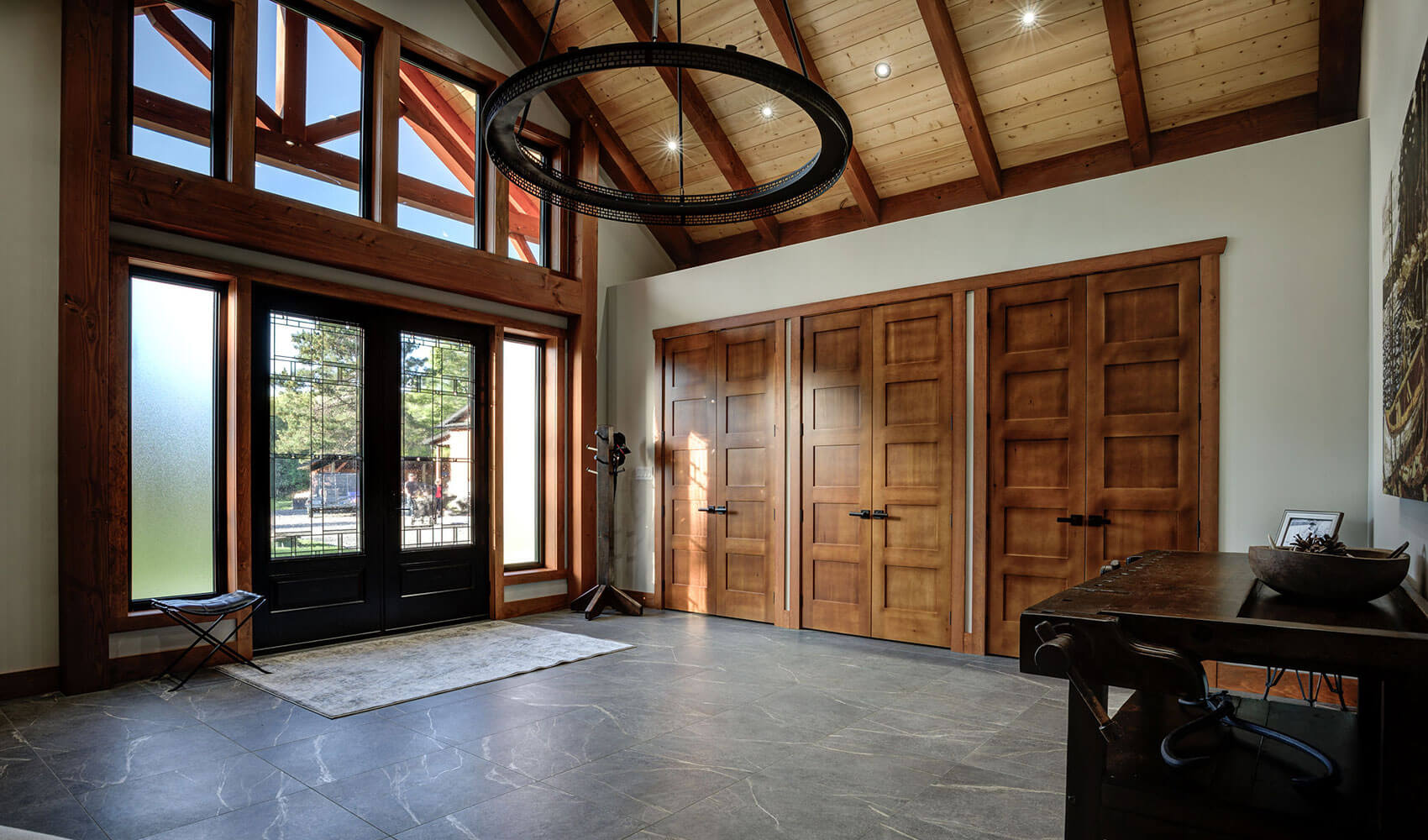 Grand timber frame entryway in a Canadian home by Smith Timber Works, featuring high ceilings, exposed wood beams, large windows, and custom wooden doors.