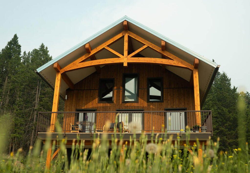 Timber frame cabin with covered balcony and exposed trusses, handcrafted by Smith Timber Works in a forest meadow.
